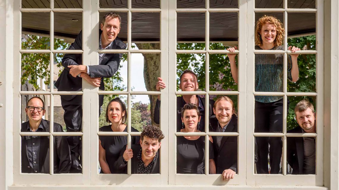 group of people standing behind a window smiling and looking through the panes