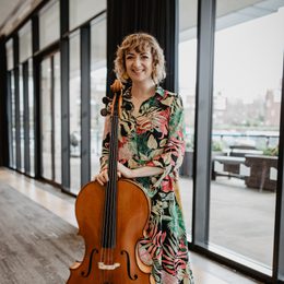 Woman standing holding a string instrument, against a background of windows