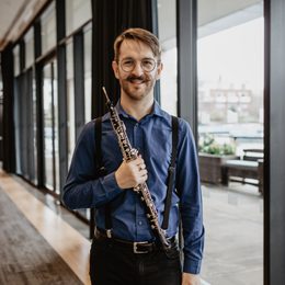 Man standing holding an instrument, against a background of windows