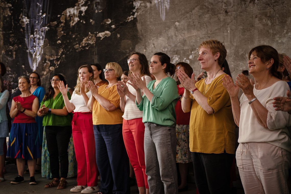 Group of women wearing bright colours and standing in a group, clapping hands.