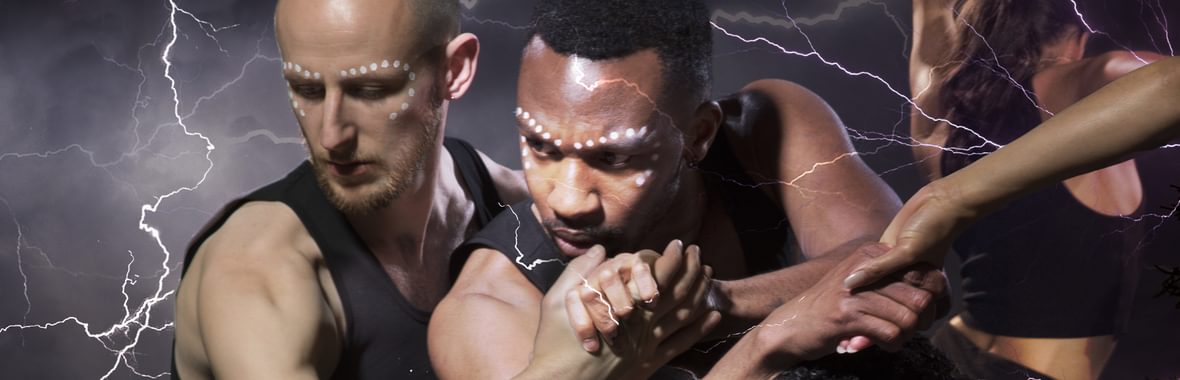 A group of dancers with hands intertwined, wearing black vests and with dotted facepaint.