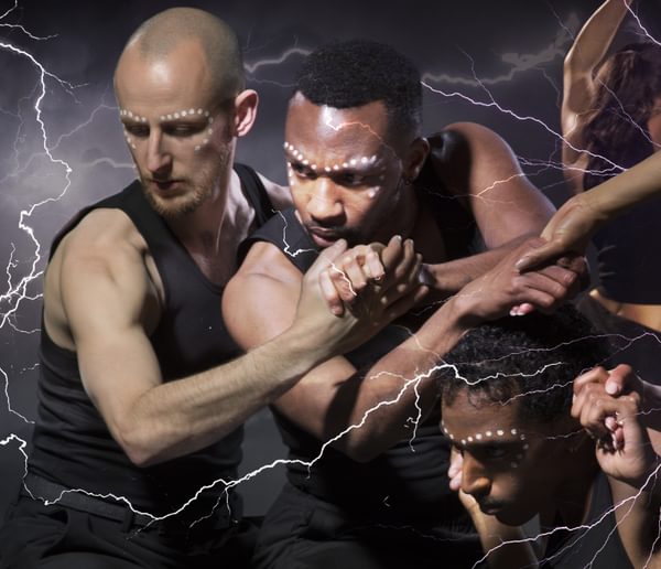 A group of dancers with hands intertwined, wearing black vests and with dotted facepaint.