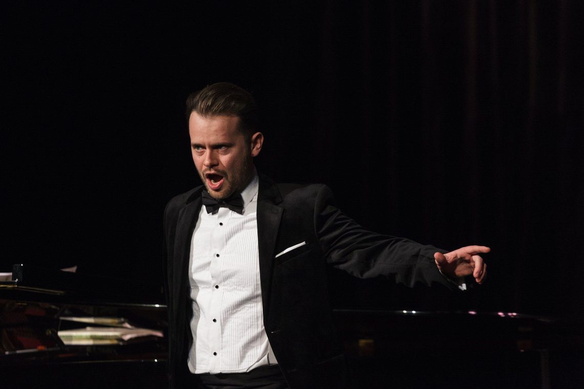 Man wearing black tie singing on stage.