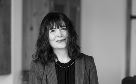 black and white image of a woman with mid-length dark hair, wearing a jacket and smiling.