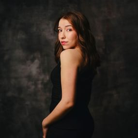 Woman with long dark hair wearing black with red lipstick, outlined by a black background.