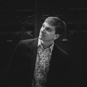 young man with short hair, wearing a patterned shirt and looking off camera.