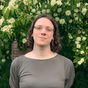 Woman with short brown hair wearing glasses standing in front of an archway of flowers.