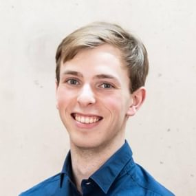 Man with light brown hair wearing a blue shirt and smiling into the camera.