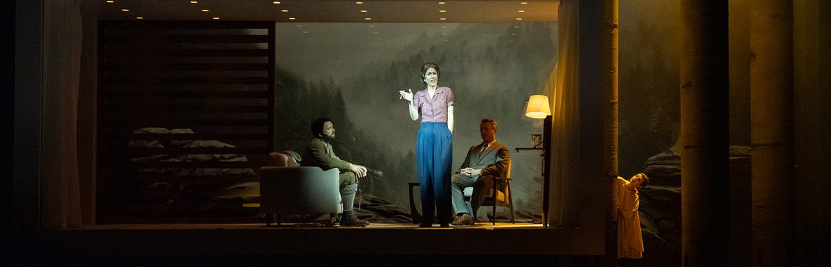 Woman standing centre stage with two men sitting either side of her