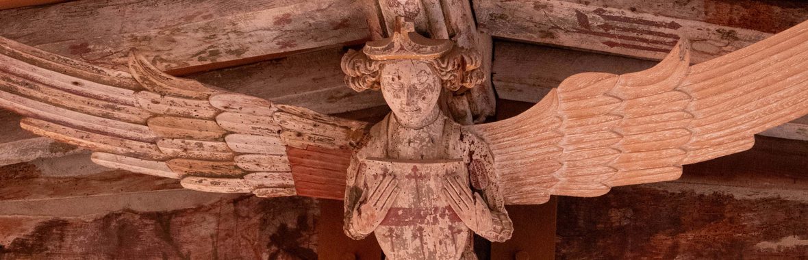 Close-up of a statue of an angel with widespread wings, wearing a crown and holding a shield