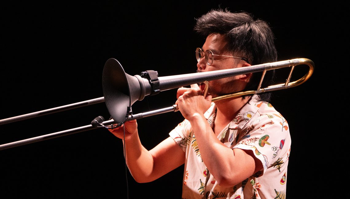 Man with short black hair playing the trombone.