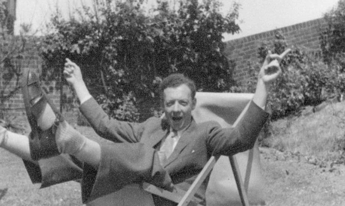 Benjamin Britten in a deckchair, in a fun pose hands in the air.