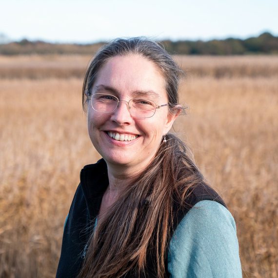 Fi Simpson smiling at the camera with reeds in the background