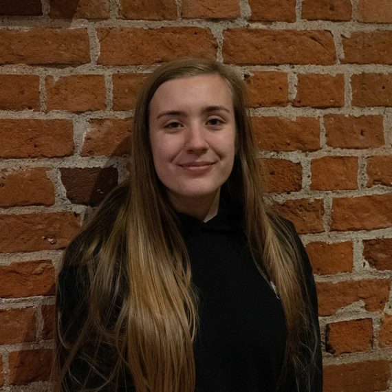 Mel Howes smiling at the camera with a brick wall in the background