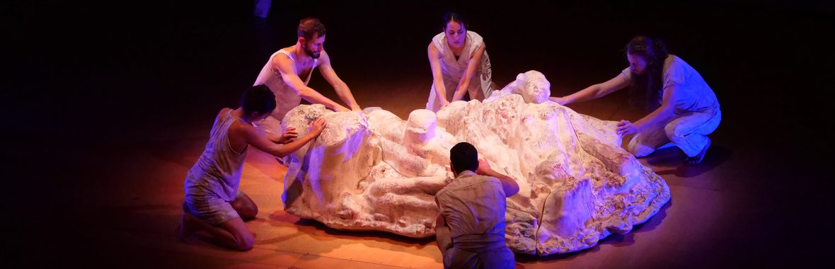 Five performers on stage in a circle around a pile of white fabric
