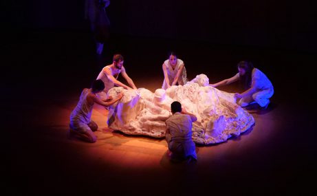 Five performers on stage in a circle around a pile of white fabric