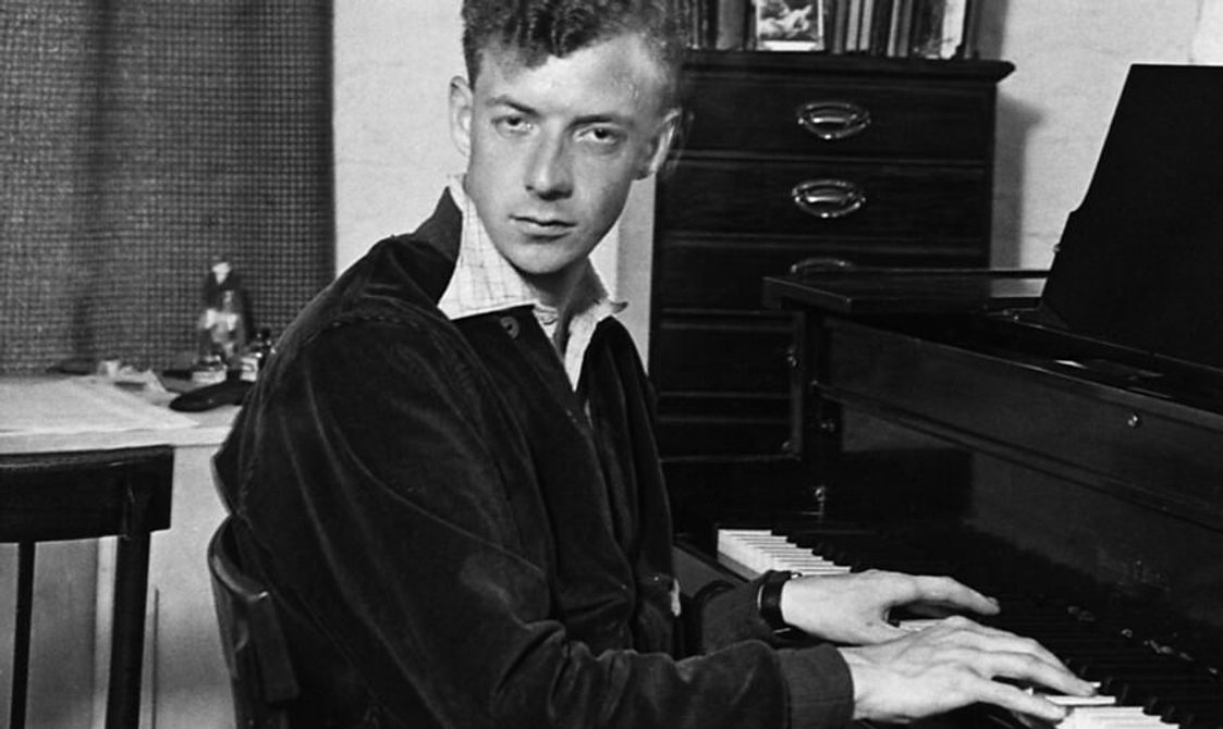black and white image of young man with short hair playing the piano and looking intensely at the camera