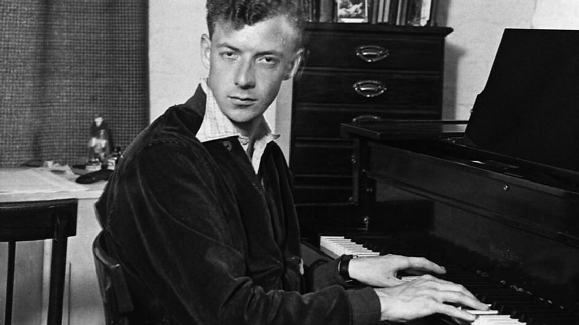 black and white image of young man with short hair playing the piano and looking intensely at the camera