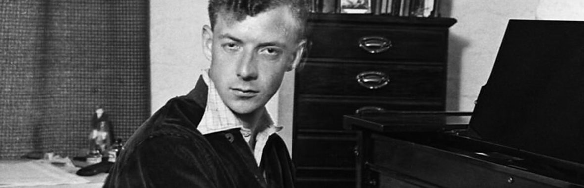 black and white image of young man with short hair playing the piano and looking intensely at the camera