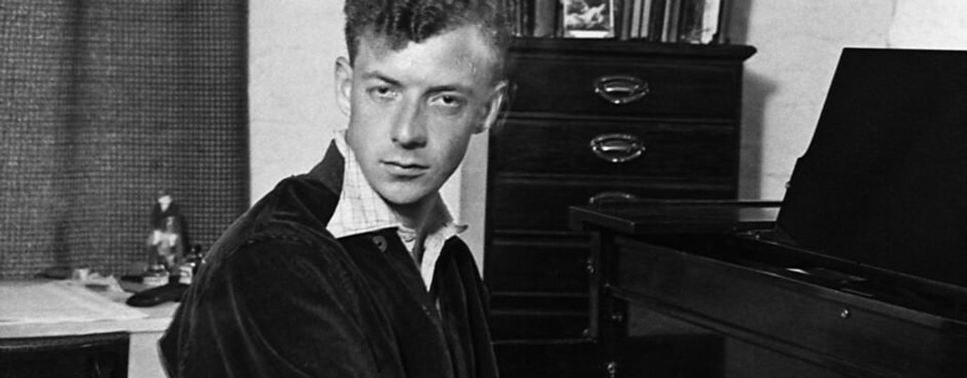 black and white image of young man with short hair playing the piano and looking intensely at the camera