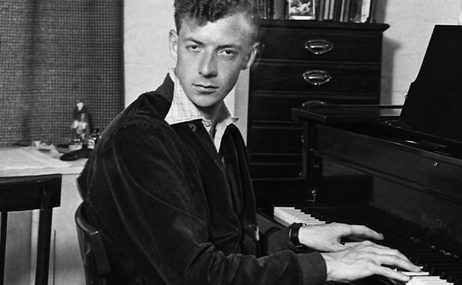black and white image of young man with short hair playing the piano and looking intensely at the camera