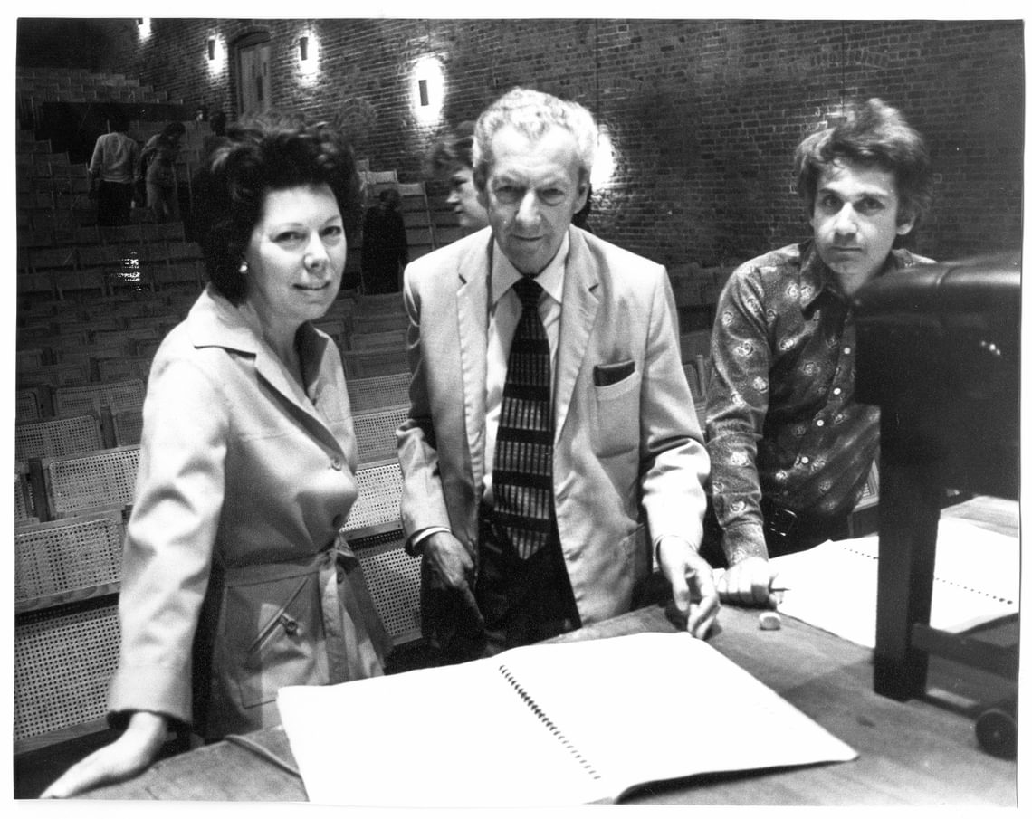 Three people in a concert hall, in front of a score resting on the stage