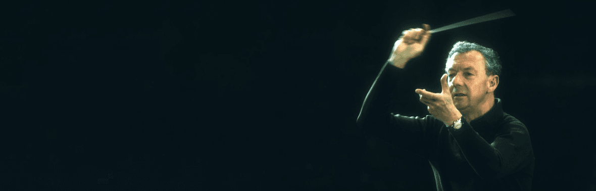 White man, in black sweater, conducting with a black background.