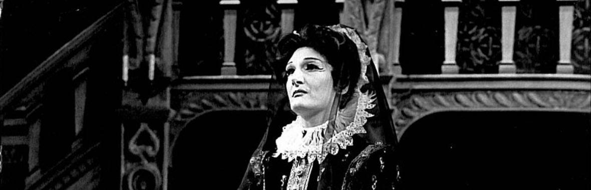 black and white view of a woman dressed in a period costume standing on a stage.