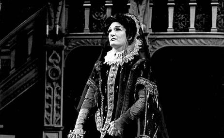 black and white view of a woman dressed in a period costume standing on a stage.