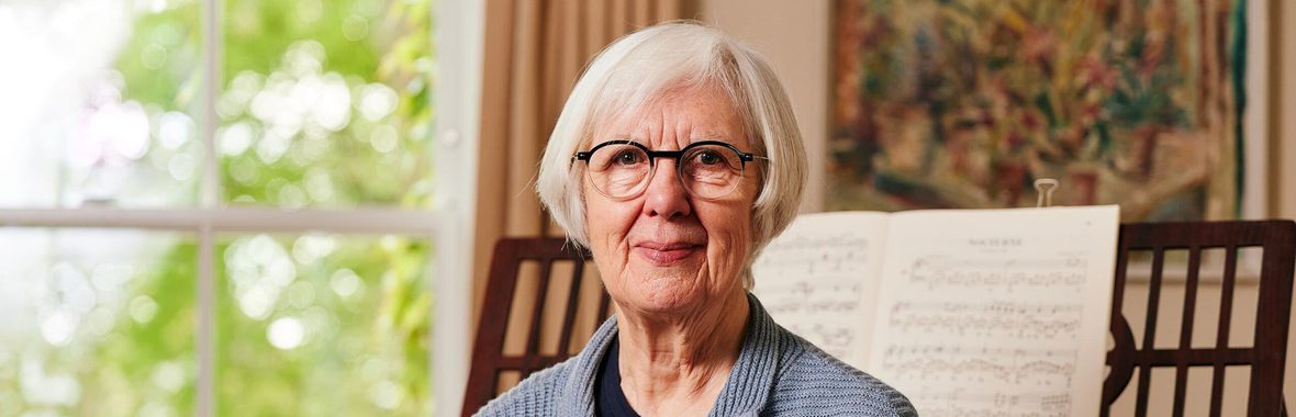 Woman sitting in front of a piano with a painting and window in the background