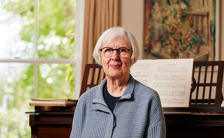 Woman sitting in front of a piano with a painting and window in the background