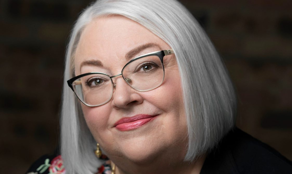 Woman with white bobbed hair and glasses looking close-up into the camera.