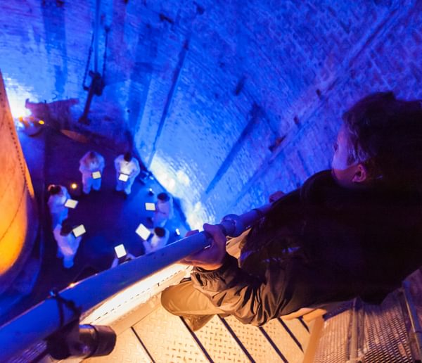 A person on a staircase overlooking a group below in blue lighting.
