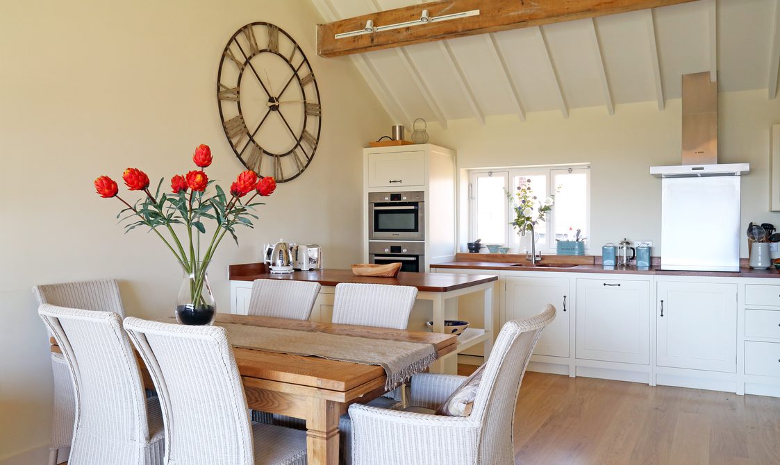 Interior view of a kitchen and dining area, six dining chairs and table with red tulips.
