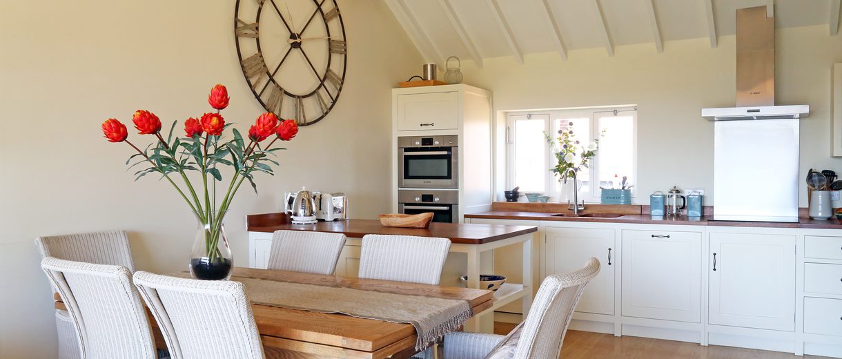 Interior view of a kitchen and dining area, six dining chairs and table with red tulips.