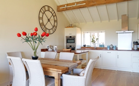 Interior view of a kitchen and dining area, six dining chairs and table with red tulips.