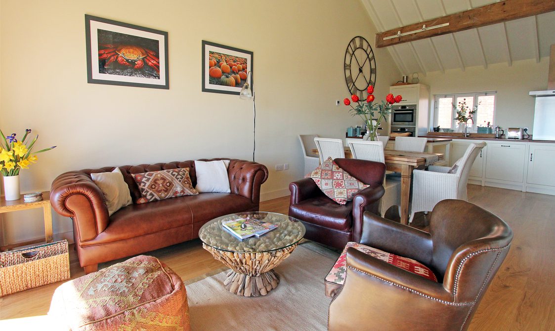 Interior view of lounge, leather chairs and sofa with dining table and kitchen in the background.