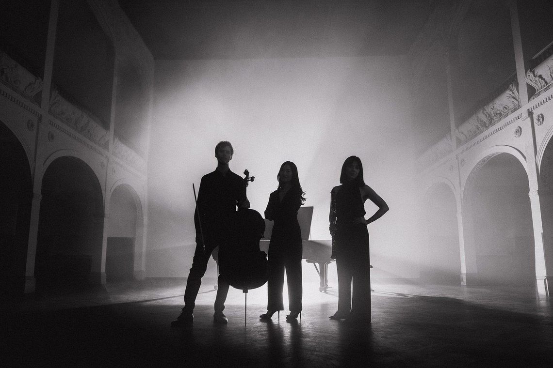 Black and white image of three musicians and their instruments standing in silhouette