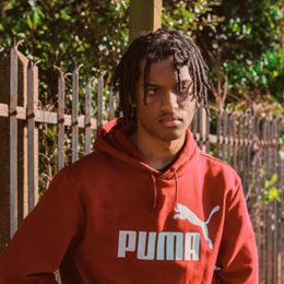 Upper body image of a young man wearing a red hoodie, outside with a wooden fence behind him
