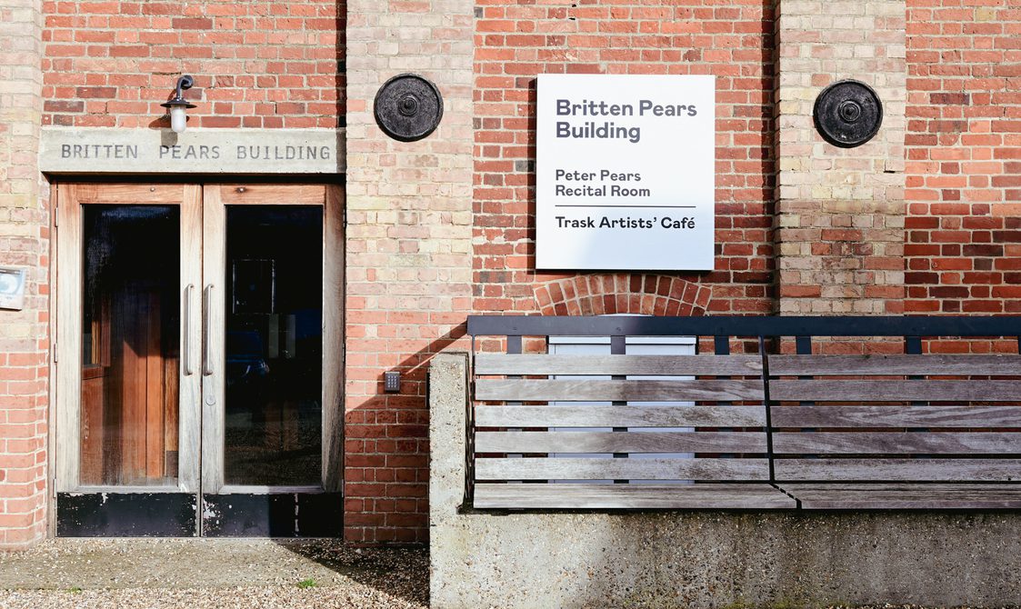 Red brick building with a wooden bench outside, and double glass entrance doors.