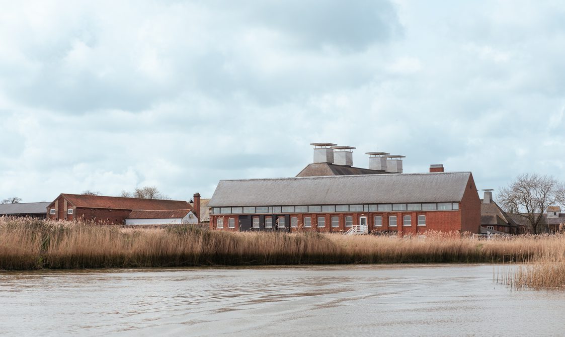 Large old maltings buildings in the distance with the river and reedbeds in the foreground.