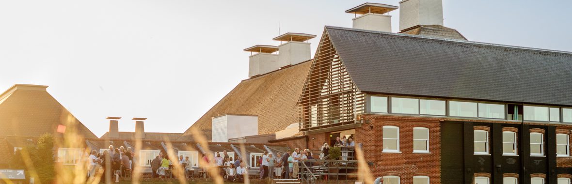 Old maltings building with people standing on the terrace, reedbeds in the foreground.