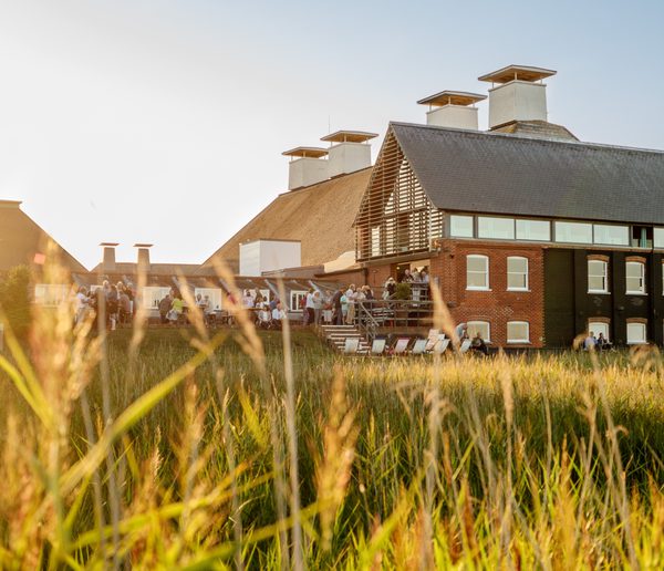 Old maltings building with people standing on the terrace, reedbeds in the foreground.