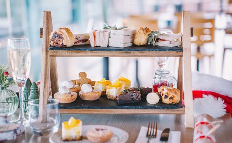 sandwiches and cakes attractively arranged on a tiered tray, surrounded by a glass of champagne and festive flowers and decorations.