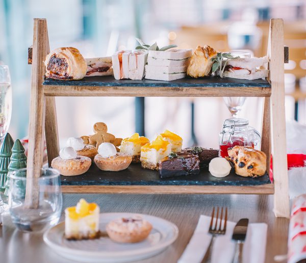 sandwiches and cakes attractively arranged on a tiered tray, surrounded by a glass of champagne and festive flowers and decorations.
