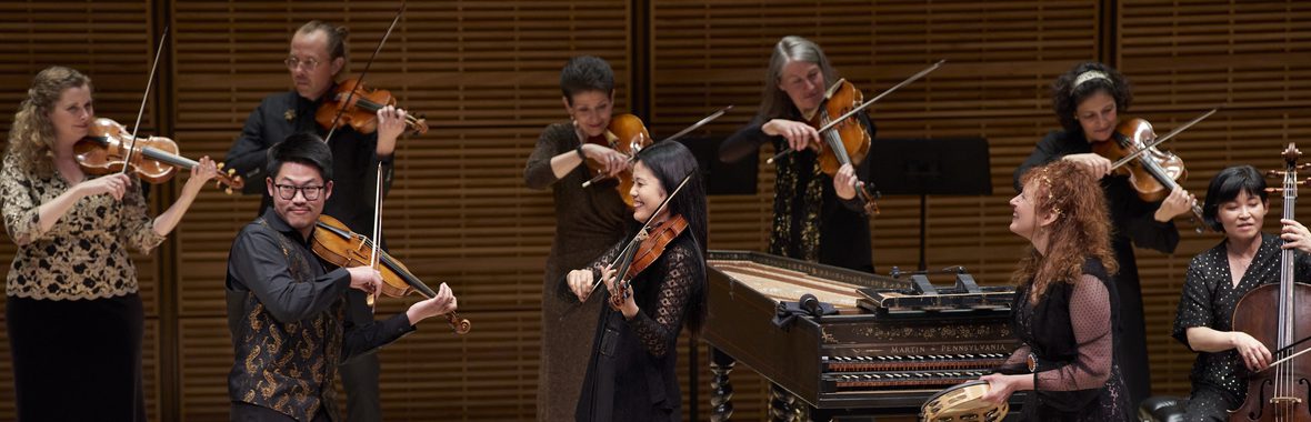 Group of musicians onstage, playing instruments and smiling.