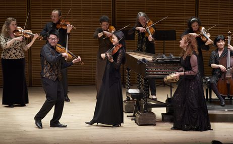 Group of musicians onstage, playing instruments and smiling.