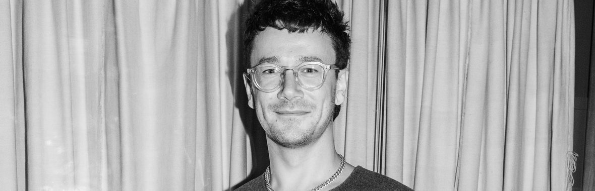 black and white photo of a man with short hair and glasses wearing a vest and smiling.