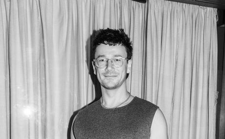 black and white photo of a man with short hair and glasses wearing a vest and smiling.