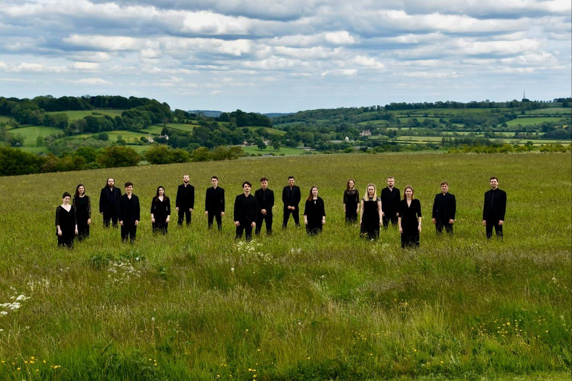 Group of men and women standing in a field wearing black clothing.